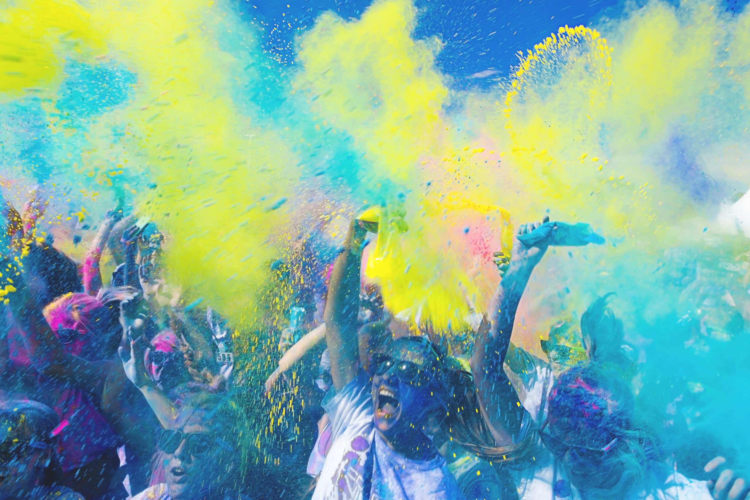 Uma explosão vibrante de cores enquanto pessoas alegres comemoram com punhados de tinta em pó nas festas universitárias, criando uma atmosfera animada e dinâmica.