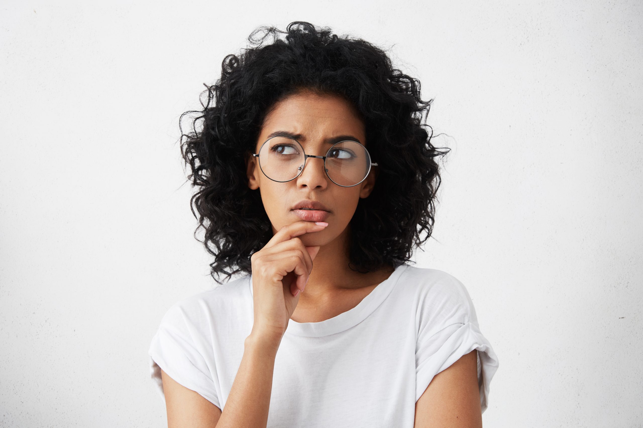 isolated-portrait-of-stylish-young-mixed-race-woman-with-dark-shaggy-hair-touching-her-chin-and-looking-sideways-with-doubtful-and-sceptical-expression-suspecting-her-boyfriend-of-lying-to-her
