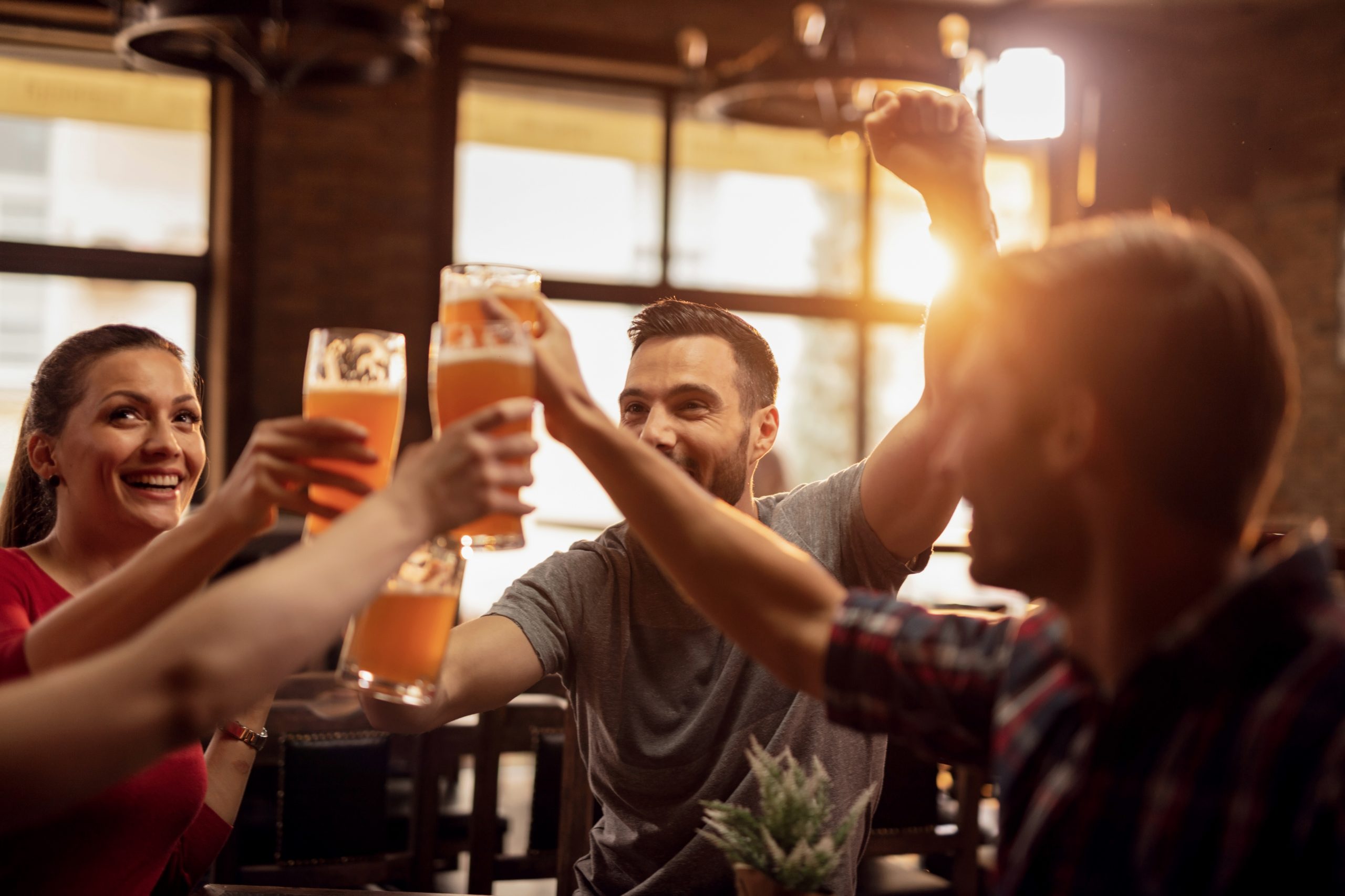 group-of-cheerful-friends-toasting-with-beer-in-a-bar