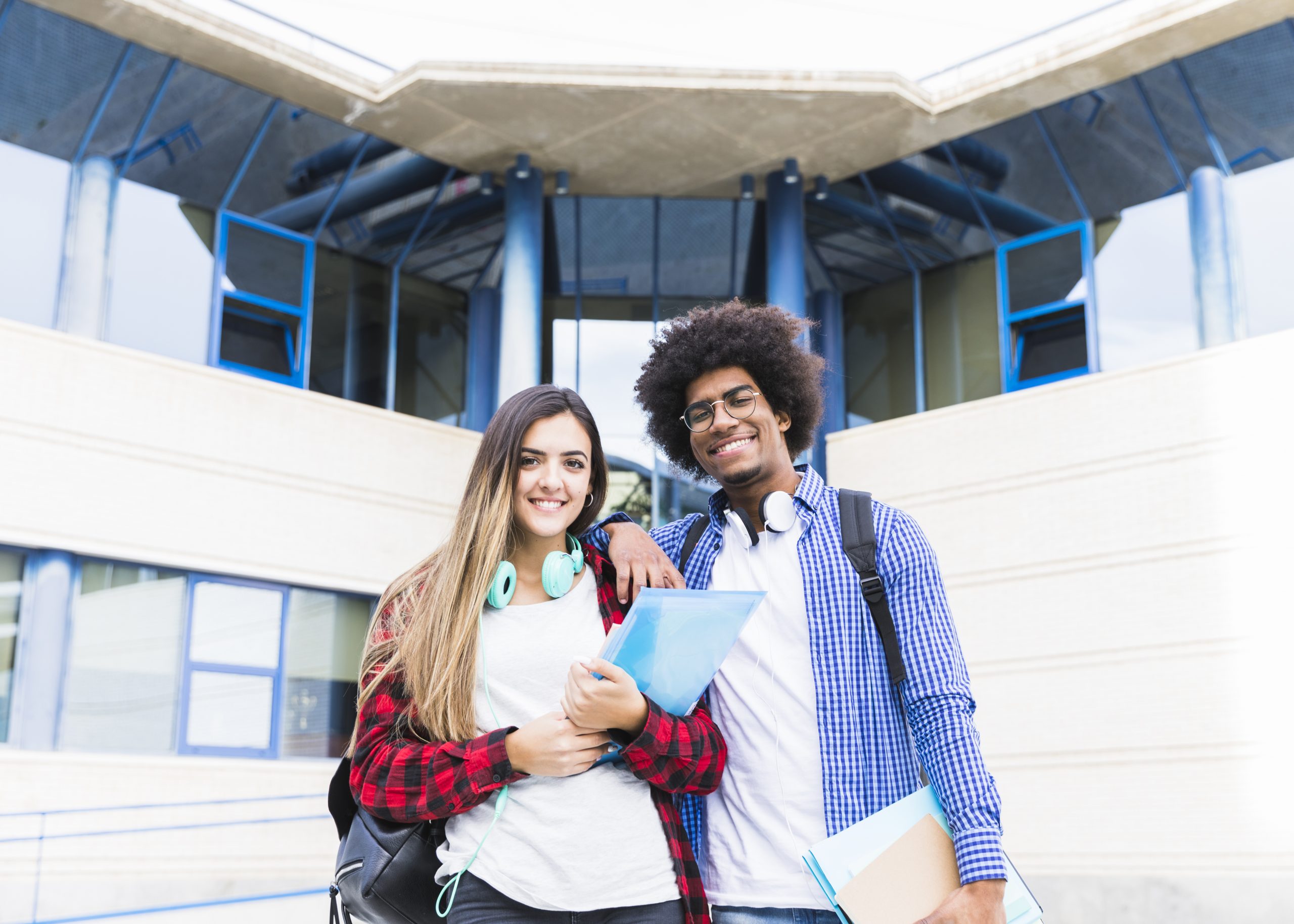 smiling-portrait-young-couple-holding-books-hand-standing-front-university-building-looking-camera