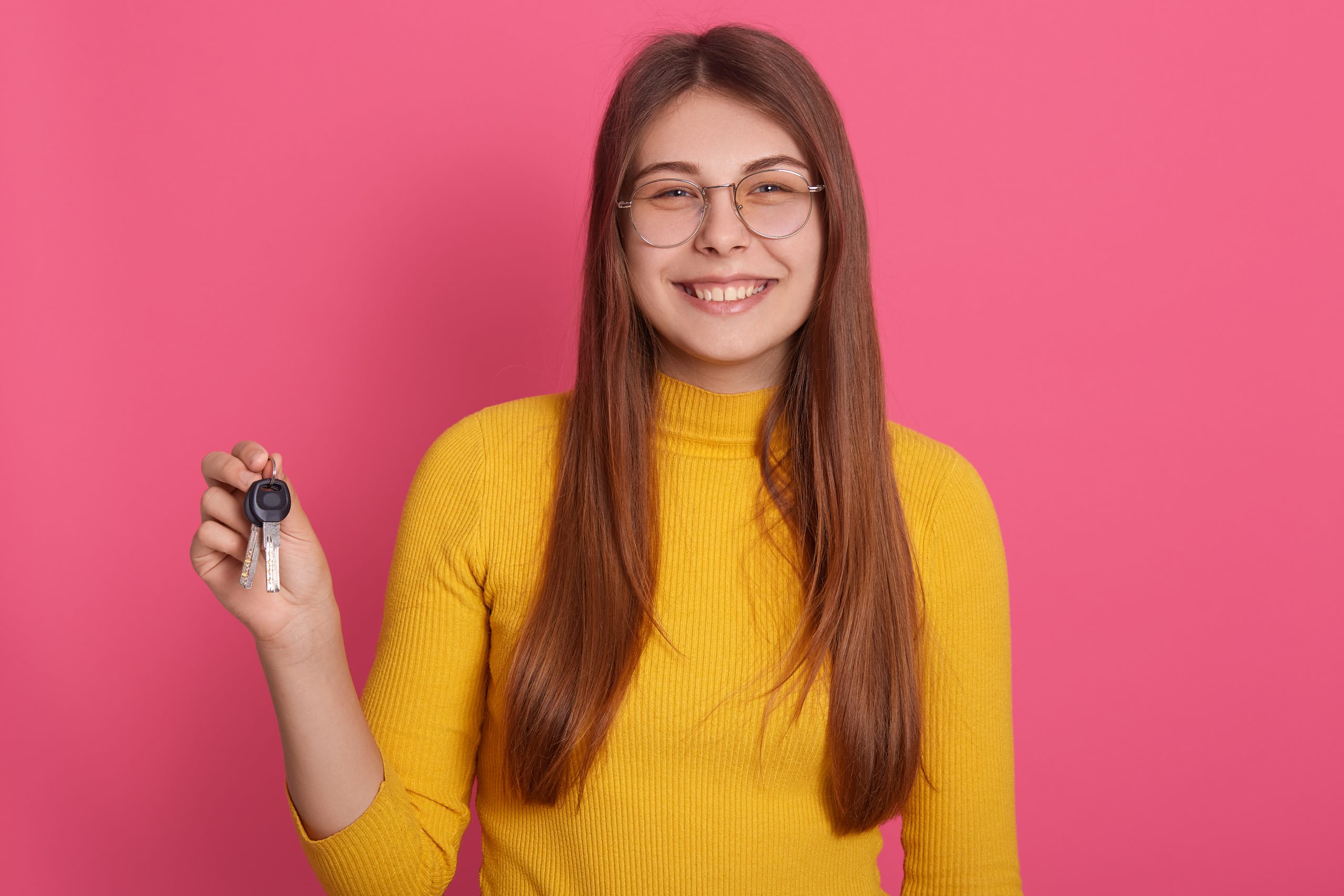 indoor-studio-image-of-adorable-magnificent-young-female-holding-keys-smiling-sincerely-looking-directly-at-camera-wearing-yellow-sweatshirt-and-spectacles-people-and-appartment-concept