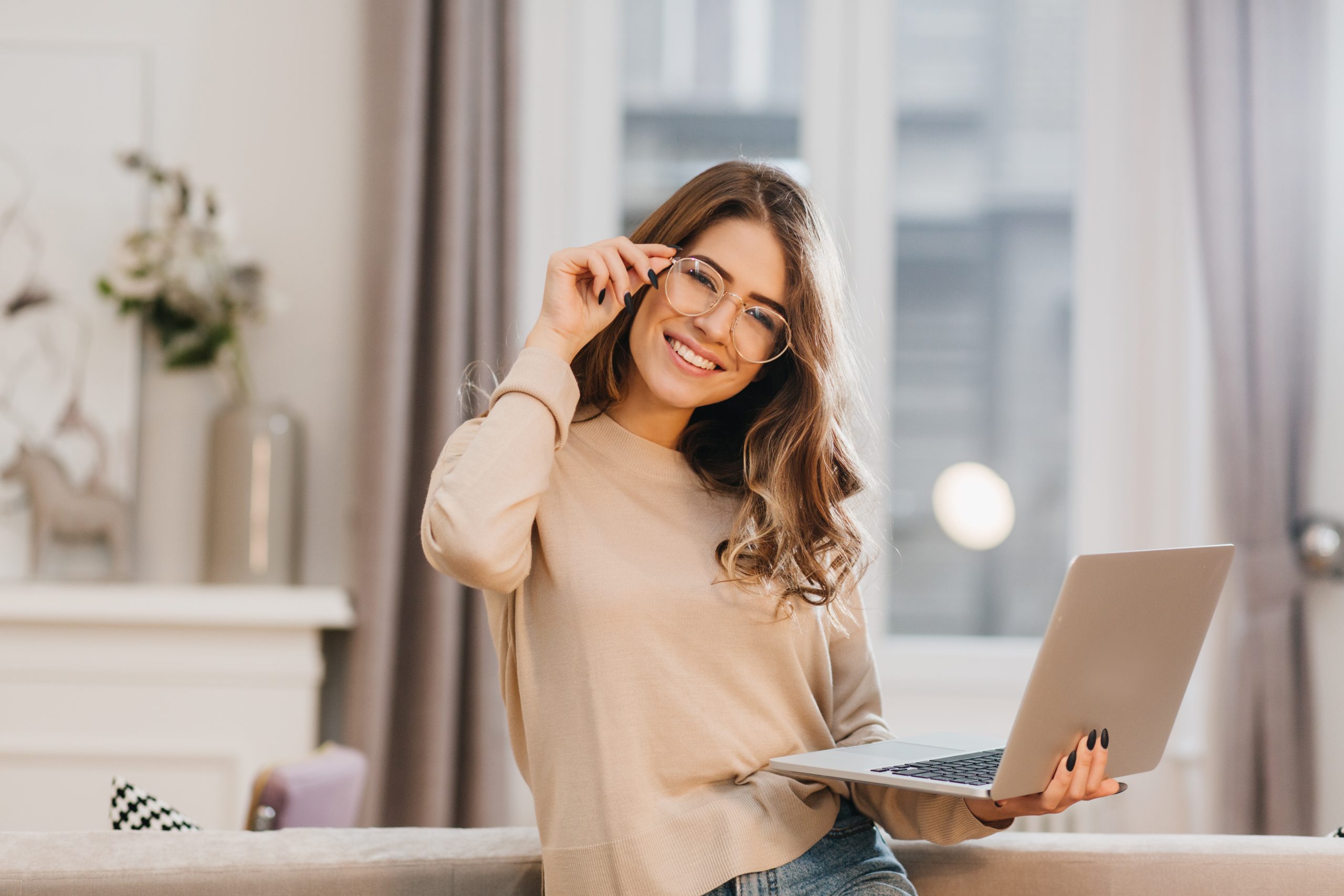 cute-girl-in-beige-shirt-touching-glasses-and-holding-laptop-with-smile-indoor-photo-of-beautiful-female-student-preparing-for-lesson-with-computer-at-home